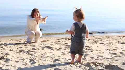 Mother and child playing on a sandy beach by the calm blue ocean water Stock Footage 345364609