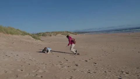 Mother and child rolling down sand dune on sunny beach Stock Footage 310192438