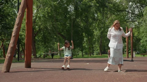 Mother and child sharing laughter while swinging under trees in park. Relaxed Stock-Footage 345143653