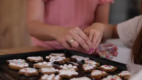 Mother and daughter adding sprinkles over Christmas cookies coated in icing Stock Footage 346684970