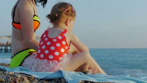 Mother and daughter are sitting on a beautiful beach and throw stones at sea Stock Footage