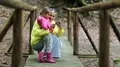 Mother and daughter in color windcheaters with cell phone on wooden bridge HD Footage