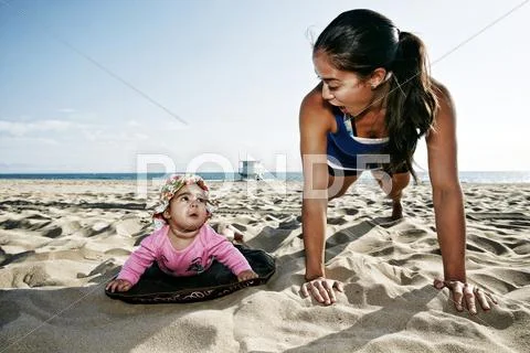 Mother and daughter doing push-ups at beach Stock Photos
