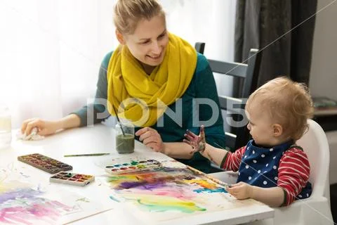 Mother and daughter doing watercolor painting - girl looking at her dirty han Stock Photos