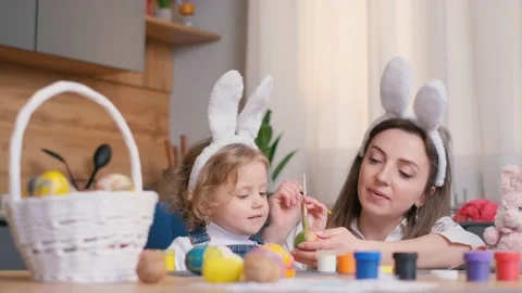 Mother and daughter draw easter eggs in the kitchen room. A happy family is Stock Footage 236209987