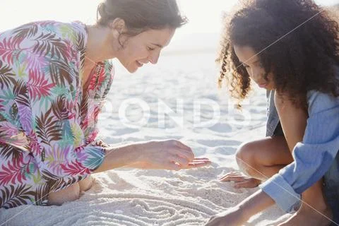 Mother and daughter drawing in sand on sunny summer beach Stock Photos