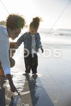 Mother and daughter drawing on wet sand on beach Stock Photos