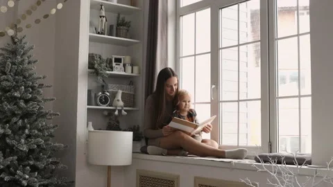 Mother and daughter having fun on Christmas morning. Young mom reading a book Stock Footage 140678853
