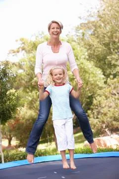 Mother And Daughter Jumping On Trampoline In Garden Stock Photos