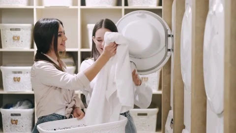 Mother and daughter loading clothes into washing machine at self service laundry Video stock 144765754