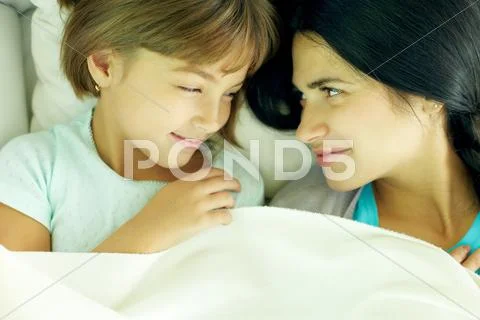 Mother and daughter lying together in bed and looking at each other Stock Photos