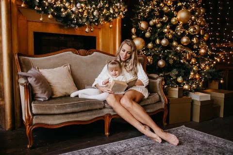 Mother and daughter reading a book at fireplace on Christmas eve. Decorated Stock Photos