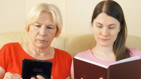 Mother and daughter reading e-book and physical print book. Concept of paper vs Stock Footage 87187655