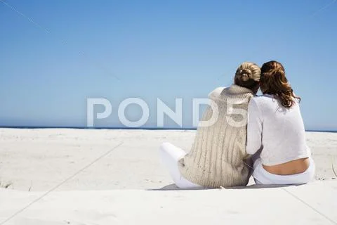 Mother And Daughter Sitting On Beach, Rear View