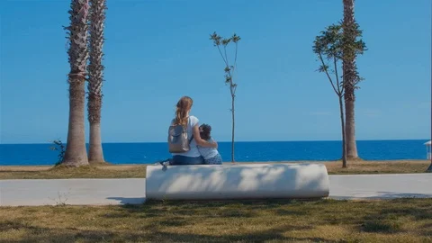 Mother and daughter sitting on a bench and looking at the sea Видео 108166324