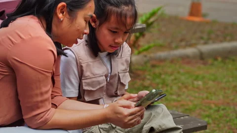 Mother and daughter using smartphone for digital learning and research in a park 库存影片 333663932