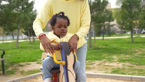 Mother and girl using a small swing in a playground Stock Footage 273551069