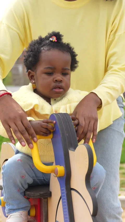 Mother and girl using a small swing in a playground Stock Footage 273740258