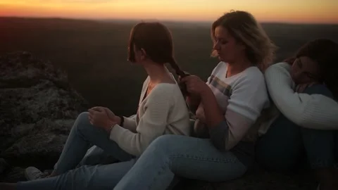 A mother and her daughters sit on top of a cliff during an incredible sunset. A Stock Footage 220559643