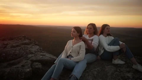 A mother and her daughters sit on top of a cliff during an incredible sunset. A Stock Footage 235603573