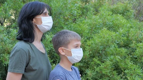 Mother and kid with medical protective masks standing in the park or forest at Stock Footage