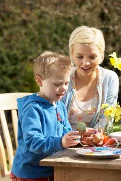 Mother and son decorating easter eggs on table outdoors Stock Photos