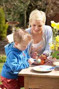 Mother and son decorating easter eggs on table outdoors Stock Photos