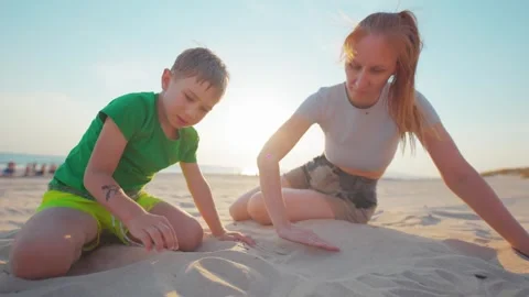 Mother and son enjoy time at the beach and build shapes in the sand under the Video stock 338301104