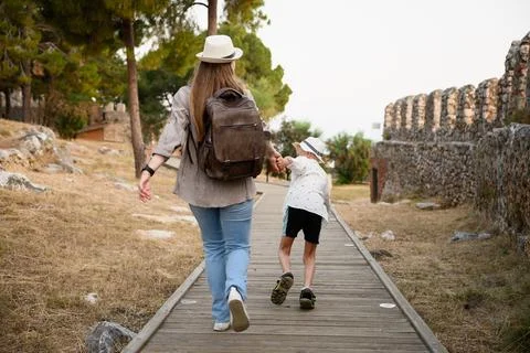 Mother and son explorers with backpack and straw hats walking on wooden path by Stock Photos
