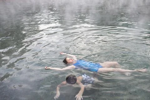 A mother and son float in Trinity Hot Springs pool with steam rising Stock Photos