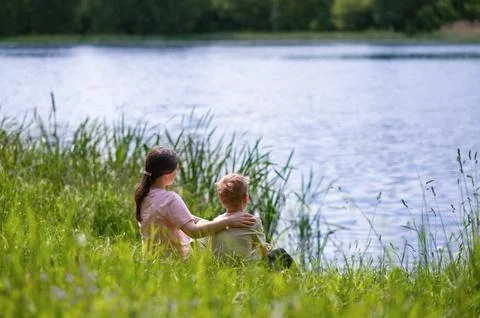 Mother and son hugging while sitting by the lake on a warm summer day, peacef Stock Photos