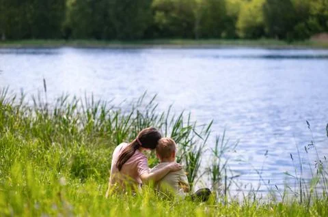 Mother and son hugging while sitting by the lake on a warm summer day, peacef Fotos de archivo