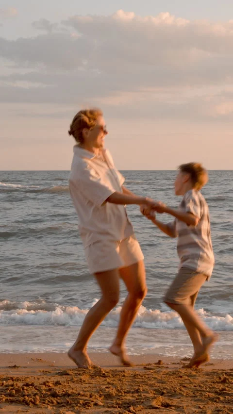 Mother and son jumping on sandy beach at sunset Stock Footage 329308567