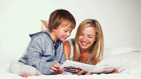 Mother and son lie in the bed and look together a family photo book Stock Footage