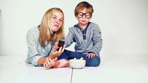 Mother and son lie on the ground and eat chips and watching tv Stock Footage