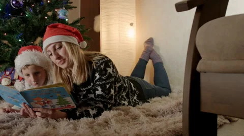 Mother and son lie under a new year tree and read a book about christmas eve Stock Footage
