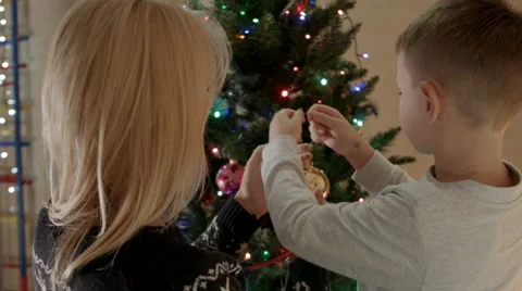 Mother and son look at each other and smiling and decorate christmas tree Vidéo 67705342