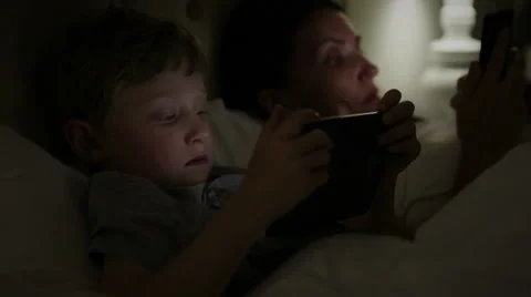 Mother and son lying in the bed reading from their electronical devices Vidéo 53671804