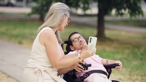 Mother and son with a physical disability taking a selfie together in a park Stock Footage 341256664
