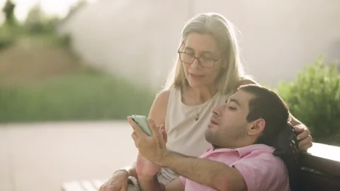 Mother and son with a physical disability using a smartphone together outdoors Stock Footage 341256697