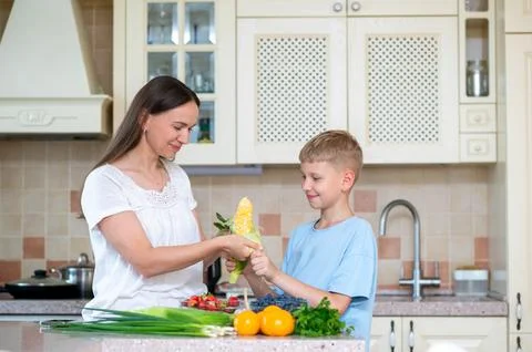 Mother and son preparing corn and vegetables in home kitchen Stock Photos