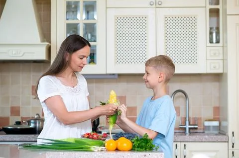 Mother and son preparing corn and vegetables in home kitchen Stock Photos