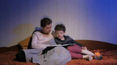 Mother and son read bedtime stories. Covered with a plaid. Flying shadows. Stock Footage 131043232