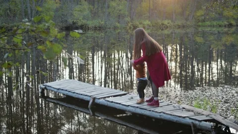 Mother and son sit and play on the pier near the forest lake Stockbeeldmateriaal 99772523