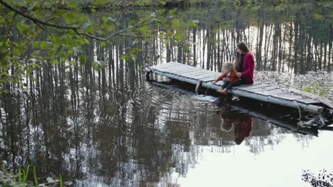 Mother and son sit and play on the pier near the forest lake Vídeo Stock 99775543