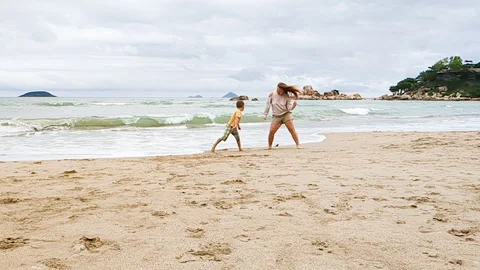 Mother and son take a fun on sea. Caucasian lady dancing on beach. Video stock 259955084