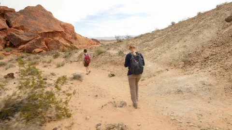 Mother and son walk down desert trail below massive rock wall Stock Footage 102145759