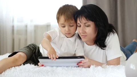 Mother and son watch a movie on a tablet computer, lying on the couch. The Stock Footage