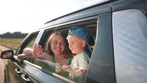 Mother and son wave from car window during road trip. Happy family travels on Stock Footage 346786317