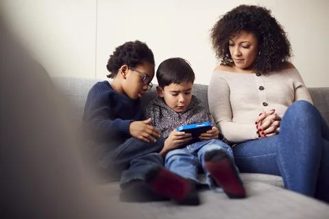 Mother And Sons Sitting On Sofa At Home Playing Computer Game Together On Hand Stock Photos